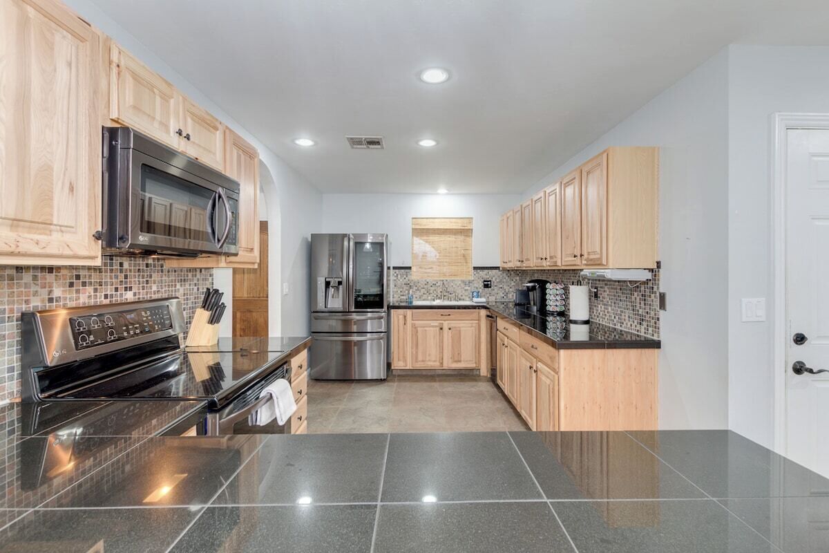 A modern kitchen with wooden cabinets, stainless steel appliances, and a black granite countertop.