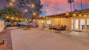 Ein überdachter Patio-Bereich mit Lichterketten, Gartenmöbeln und einem Baum.