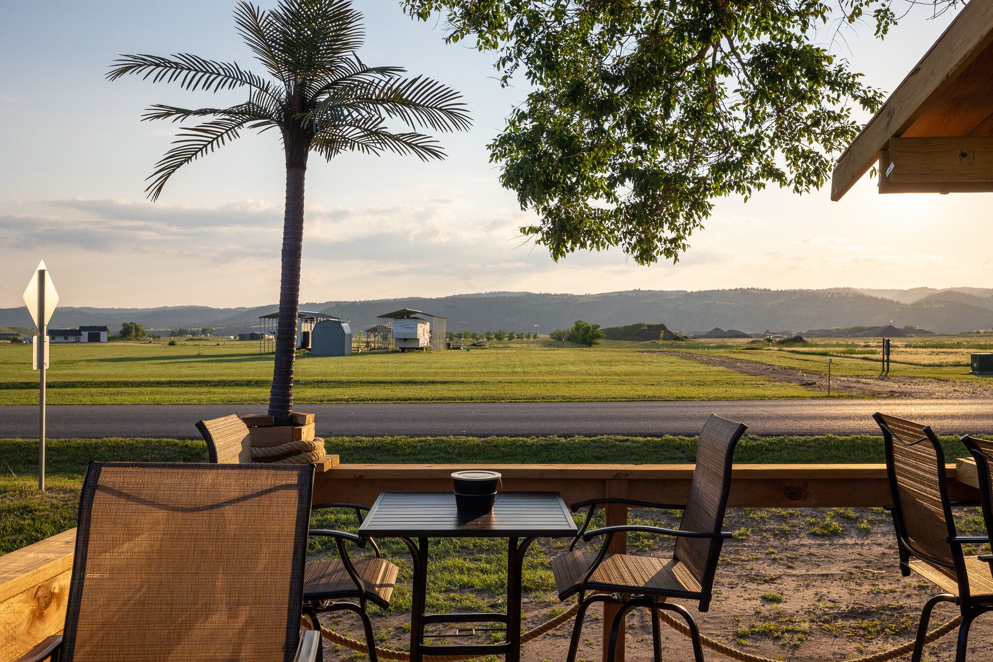 Een terras met rieten stoelen en een tafel, met uitzicht op een groen veld en verre bergen.