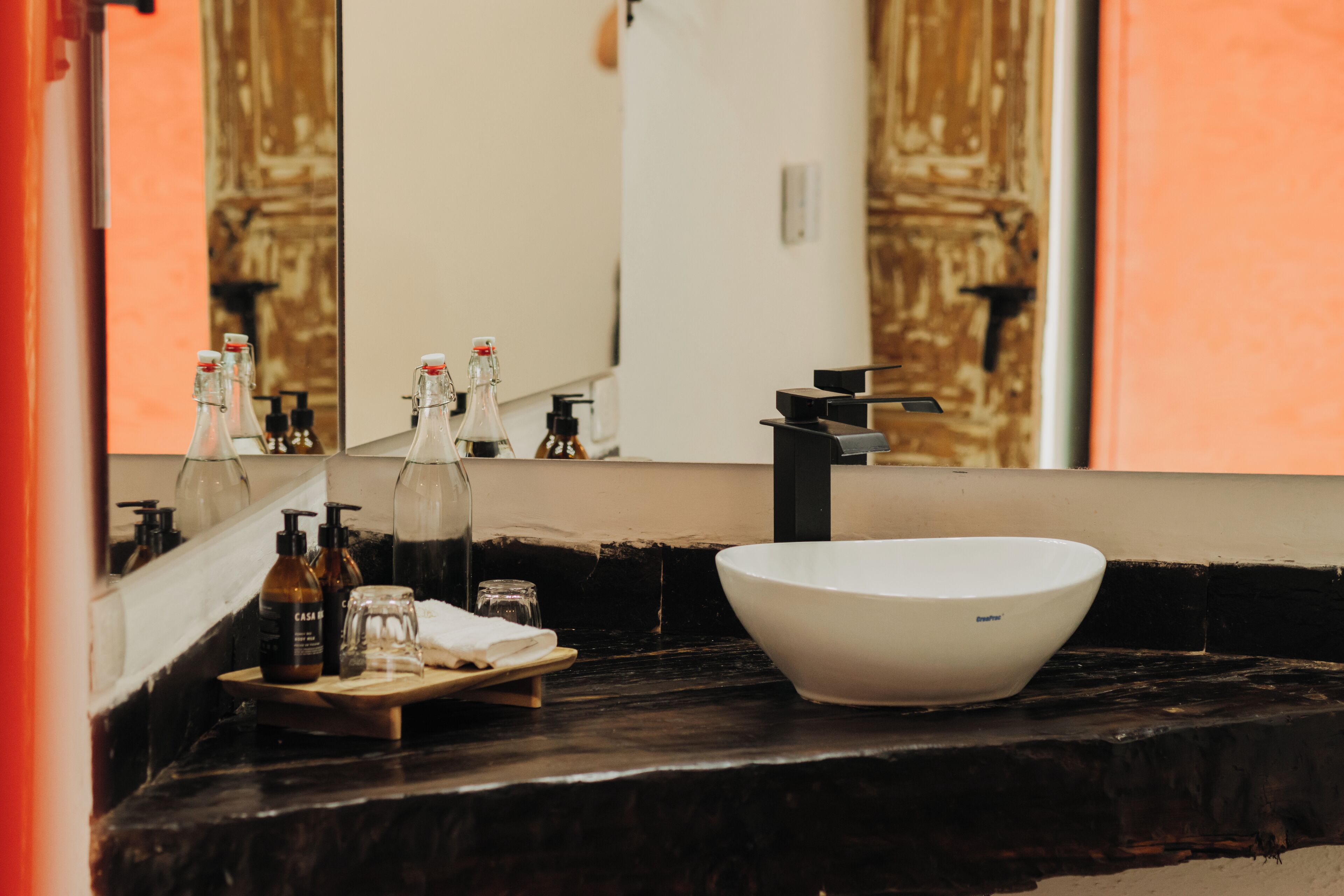 Un baño con un lavabo blanco, un espejo y varios artículos de aseo en la encimera.