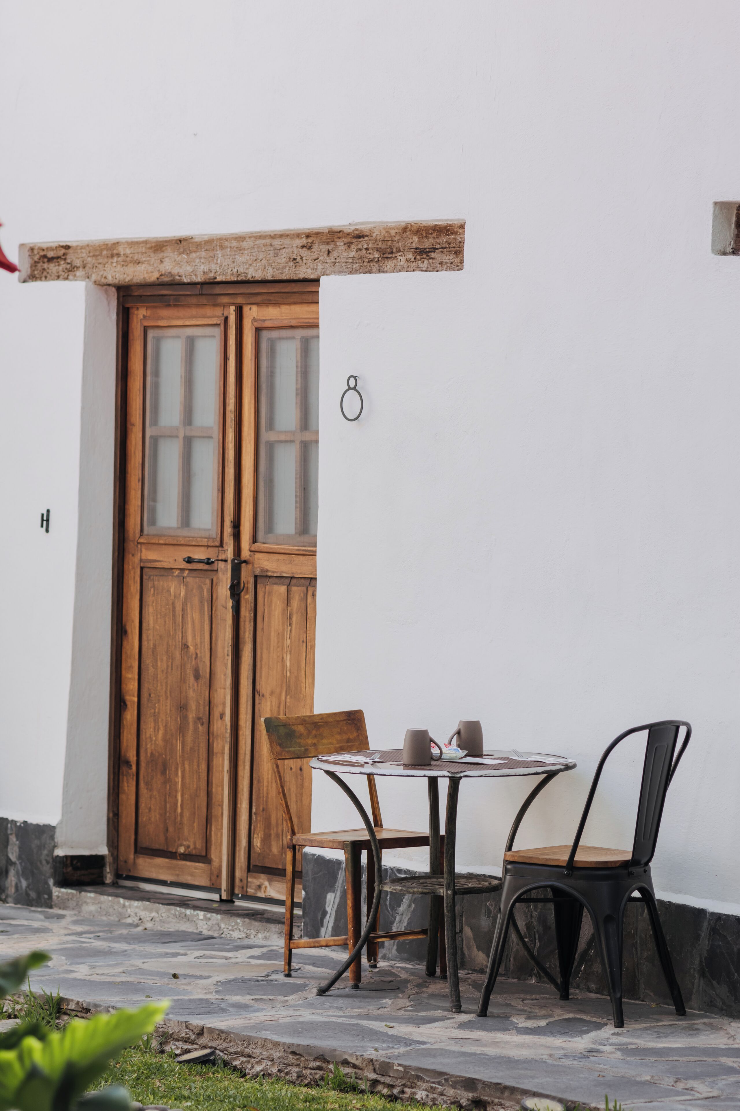 A wooden door with glass panels, a small table with two chairs, and a stone-paved area.