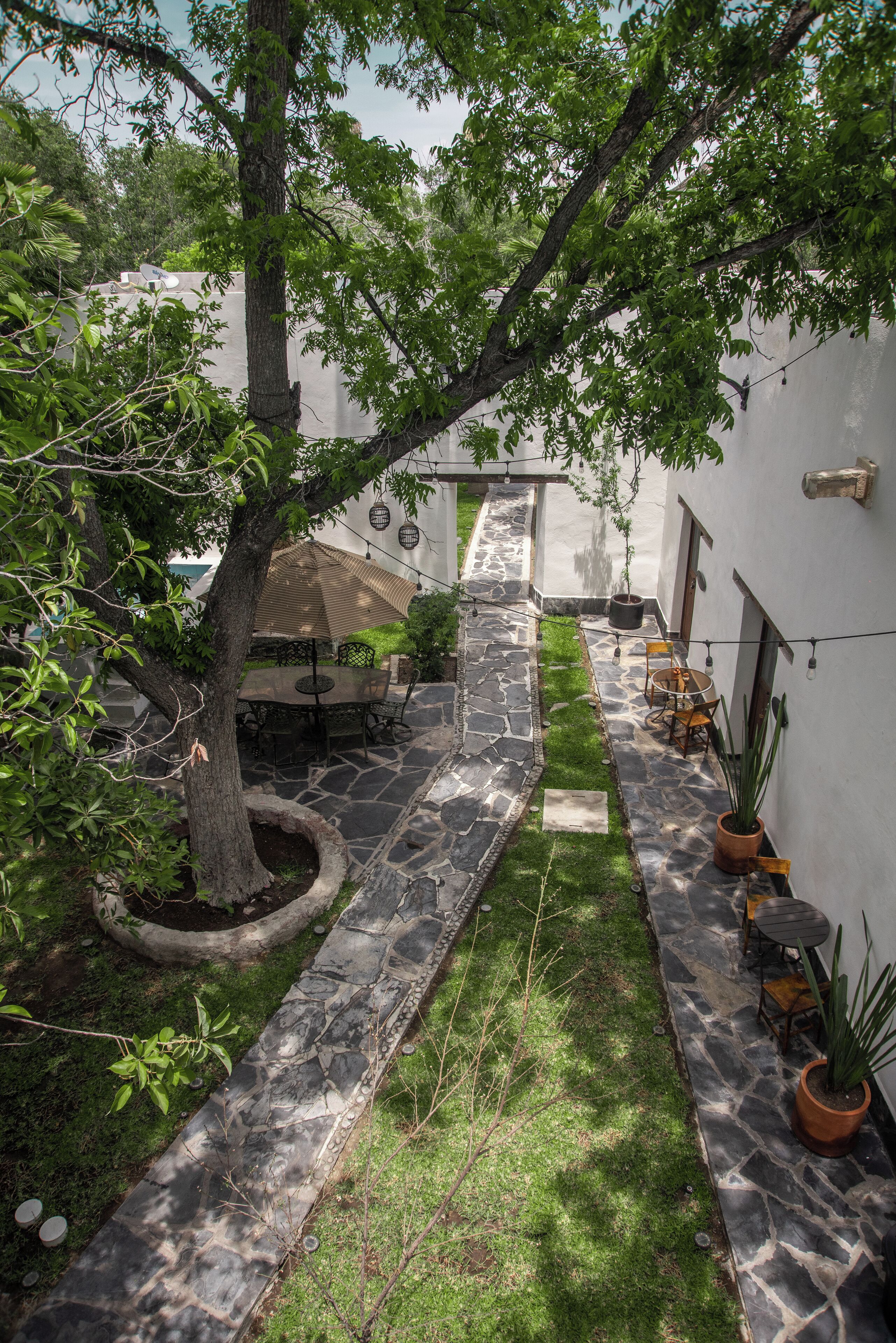 A courtyard with a stone pathway, a tree, and outdoor seating area with tables and chairs.