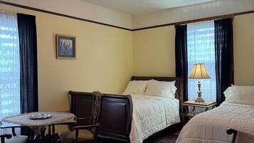 A hotel room with a bed, a desk with a chair, a small table, a lamp, and a patterned carpet.