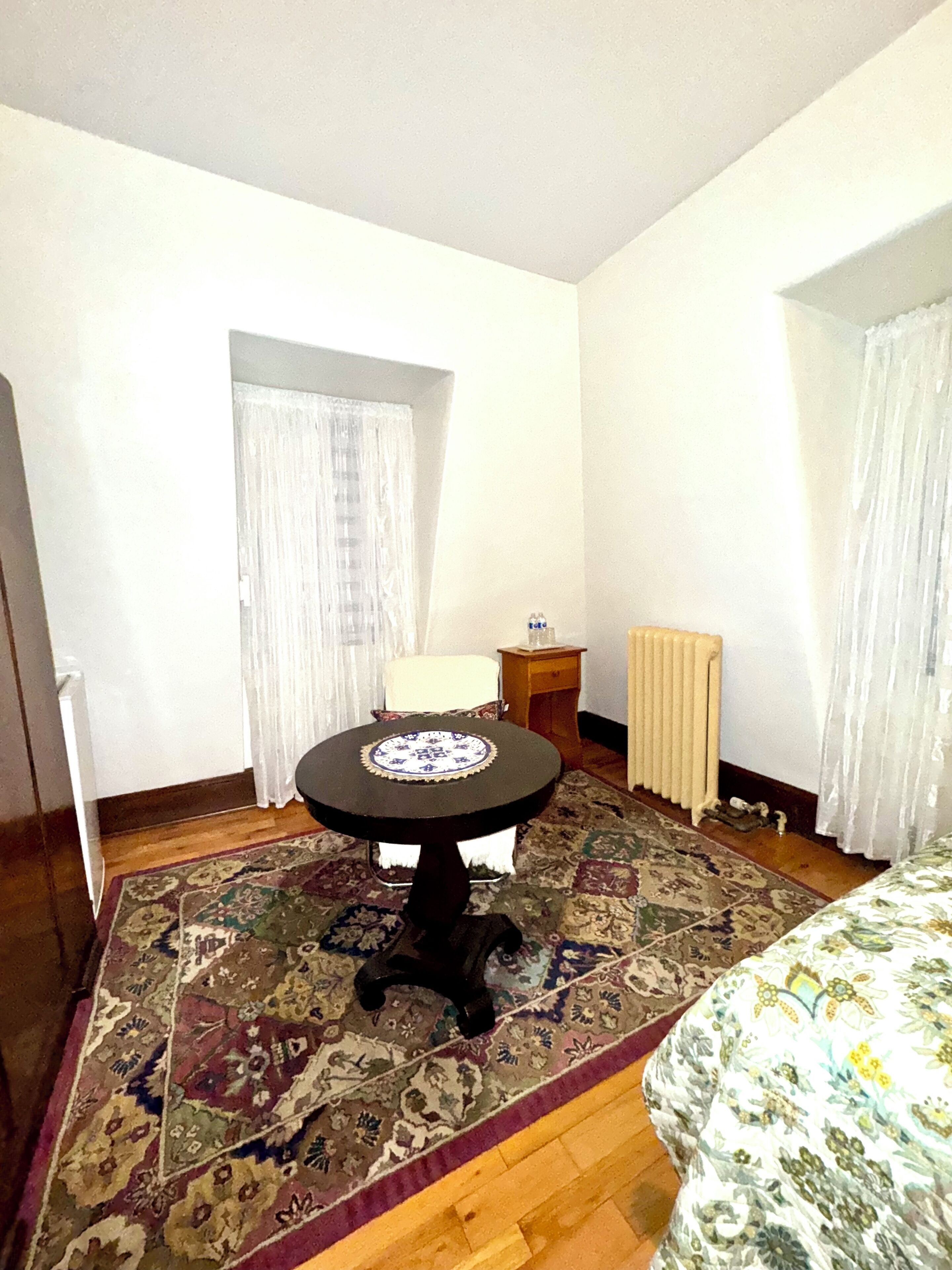 A bedroom with a round table, a bed, a radiator, and a patterned rug.