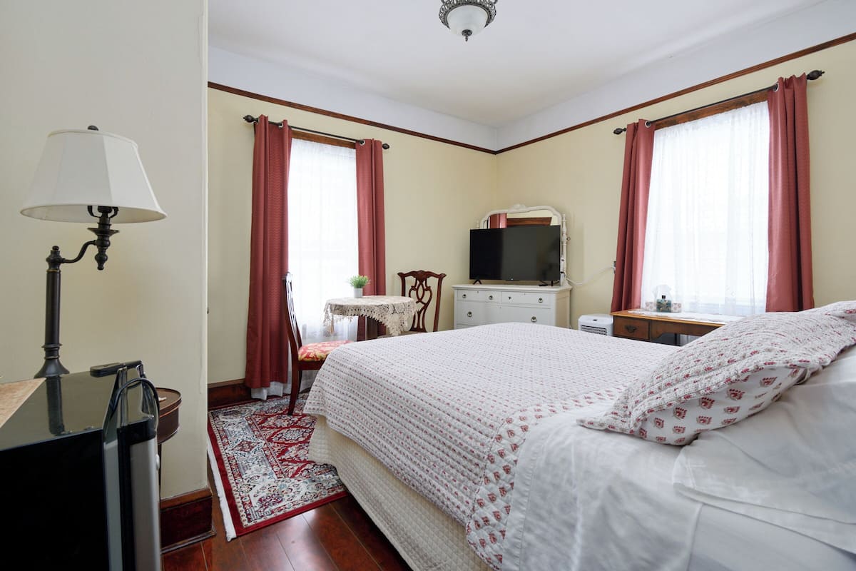A neatly arranged bedroom with a bed, a desk, a television, and a chair.