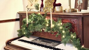 Un piano de cola con una guirnalda festiva, un reloj decorativo y un árbol de Navidad dorado sobre una repisa.