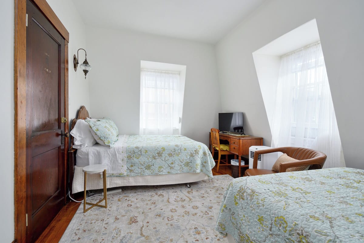 A bedroom with two beds, a desk, a chair, and a wardrobe.