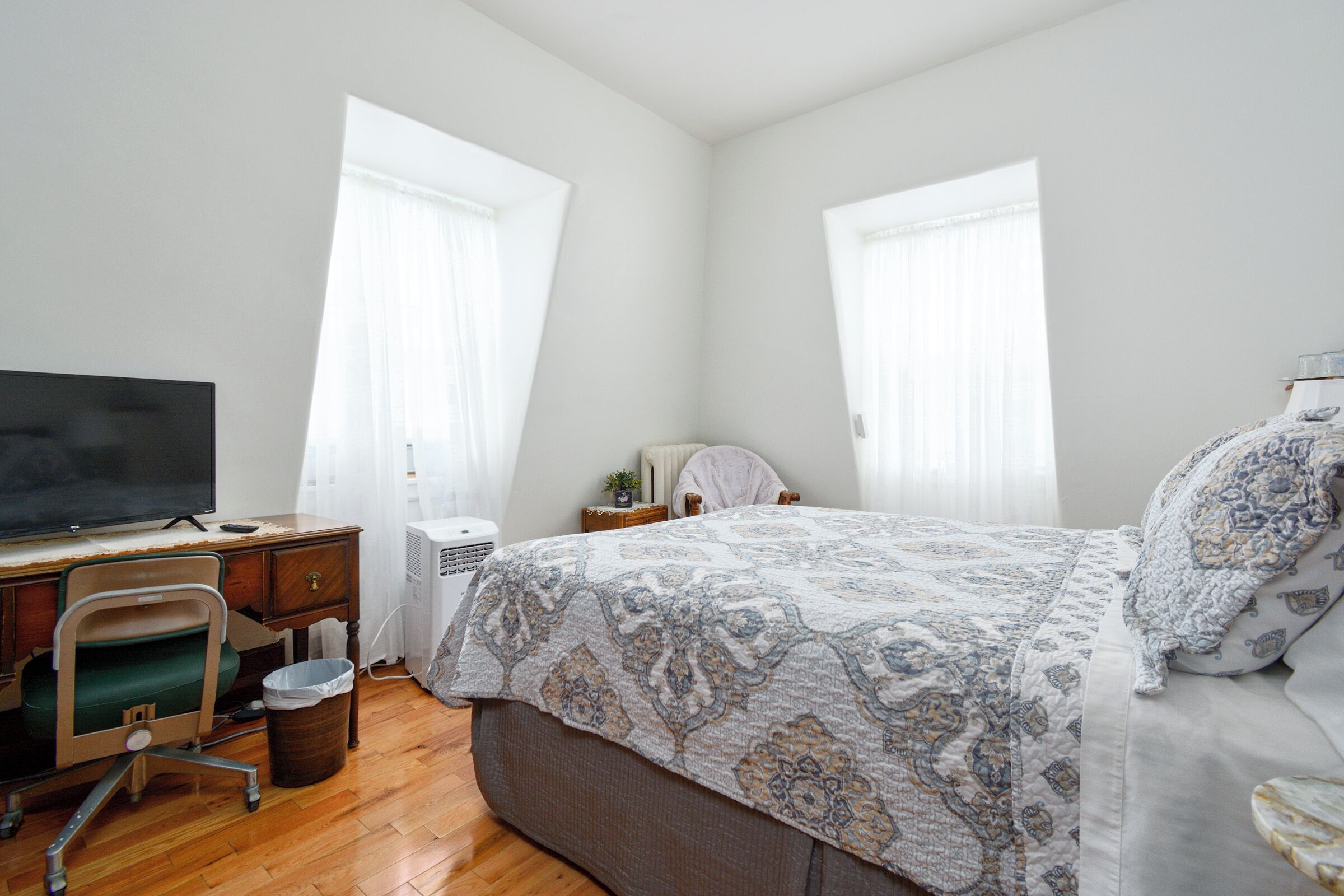 A bedroom with a bed, a desk with a computer, a chair, and a TV.