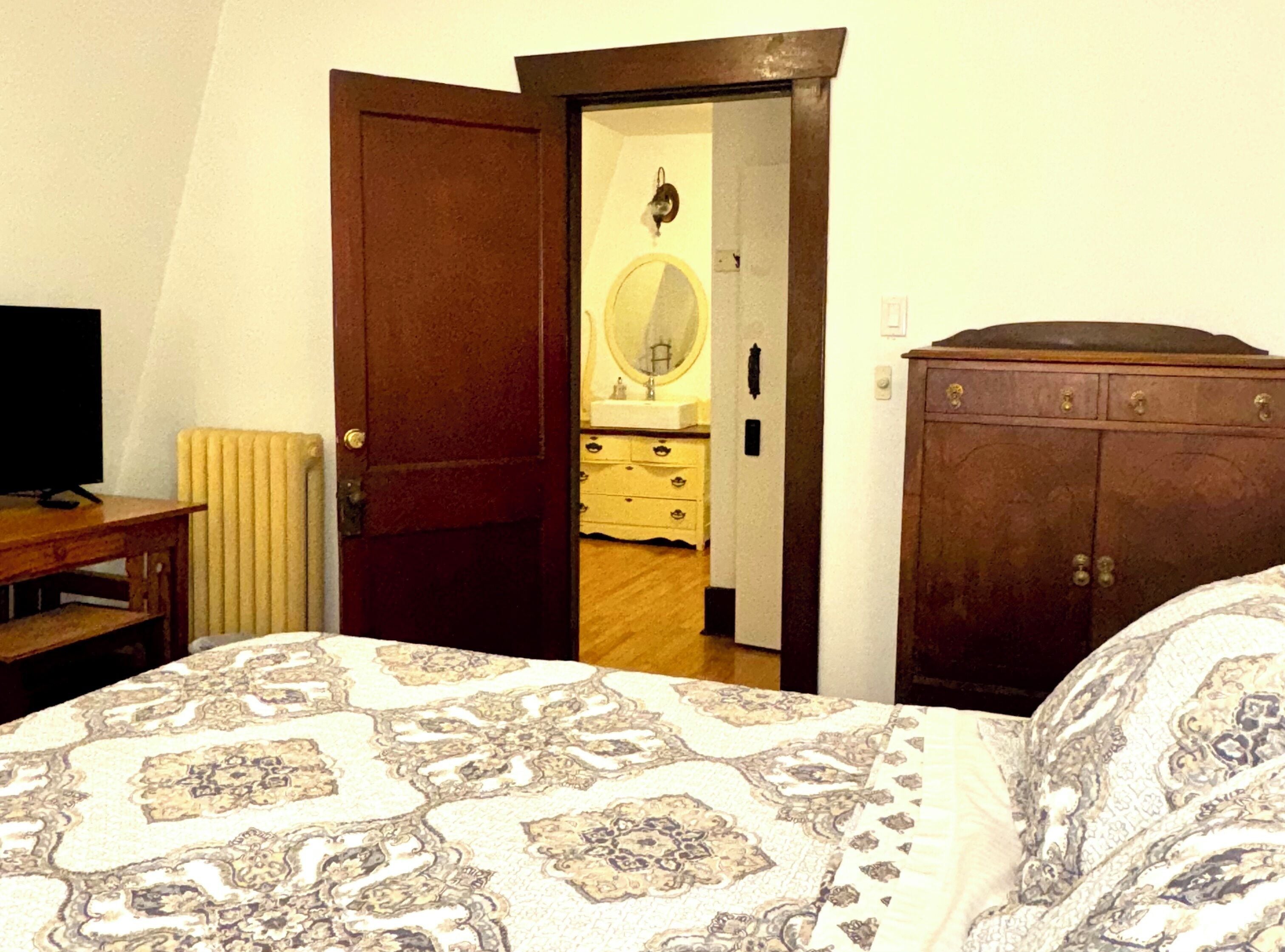 A bedroom with a bed, a wooden dresser, a mirror, and a television.