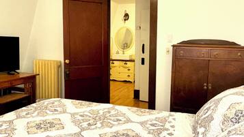 A bedroom with a bed, a wooden dresser, a mirror, and a television.
