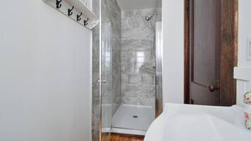 Un baño con cabina de ducha de vidrio, un lavabo blanco y una puerta de madera.