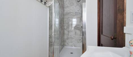 A bathroom with a glass shower enclosure, a white sink, and a wooden door.