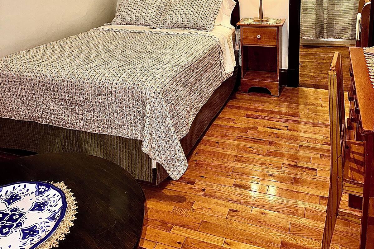A bedroom with a bed, bedside table, lamp, and a view of a hallway.