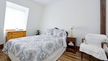 Un dormitorio con una cama grande, mesita de noche de madera, mesilla auxiliar y una silla.
