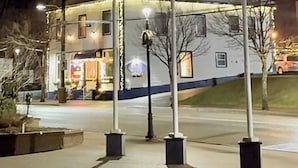 Un edificio de varios pisos con fachada blanca y detalles azules, que cuenta con un local comercial en la planta baja con letreros iluminados.