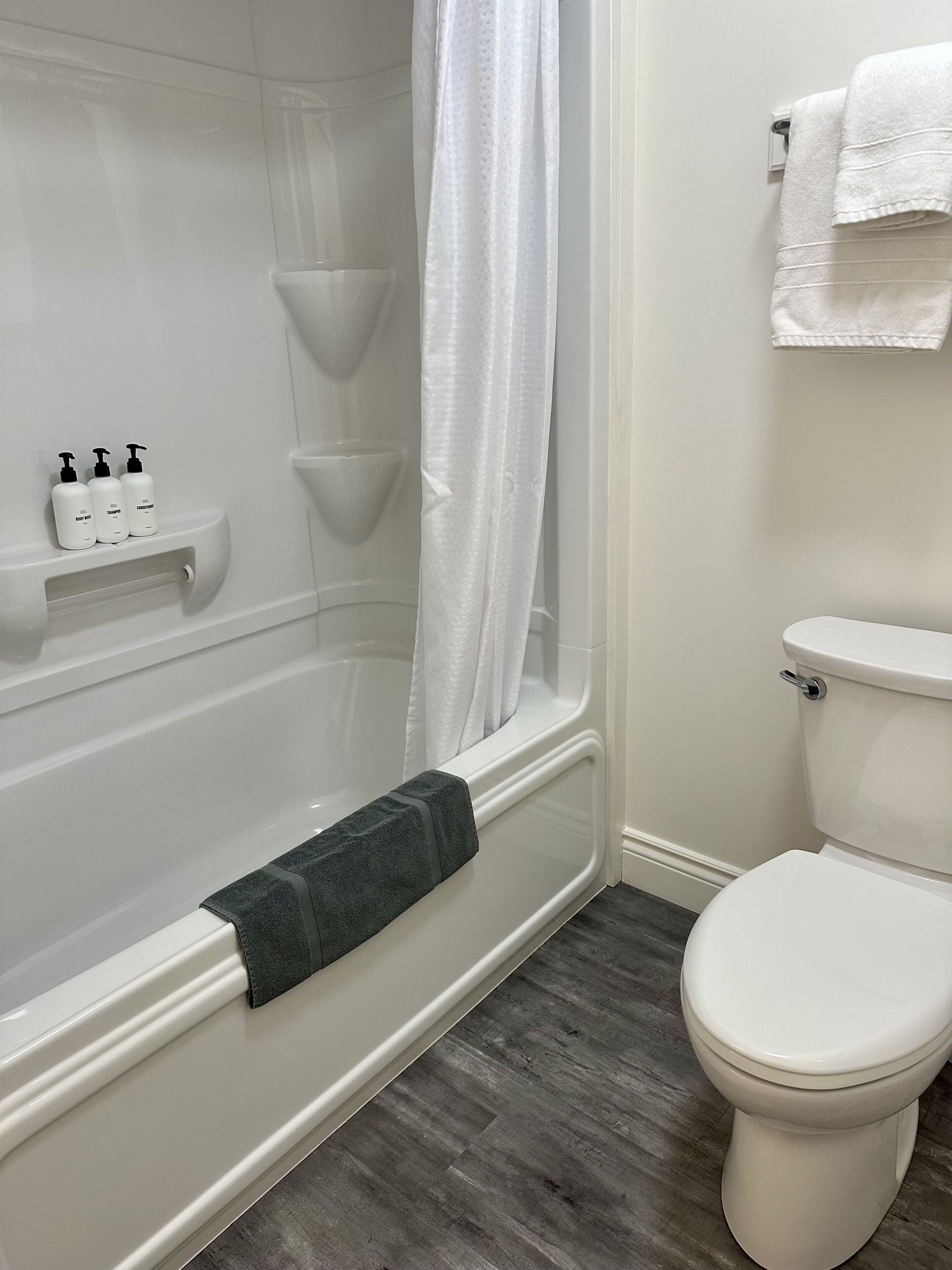 Et badeværelse med badekar, toilet og en hylde med toiletartikler.