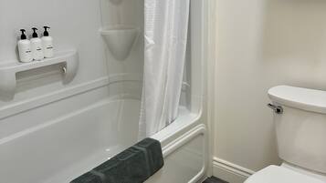 Et badeværelse med badekar, toilet og en hylde med toiletartikler.