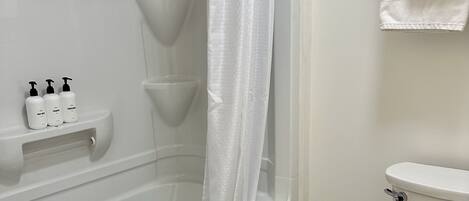 A bathroom with a bathtub, toilet, and a shelf with toiletries.