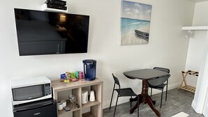 Um espaço compacto com televisão de tela plana, micro-ondas, cafeteira e área de refeições com mesa e cadeiras.
