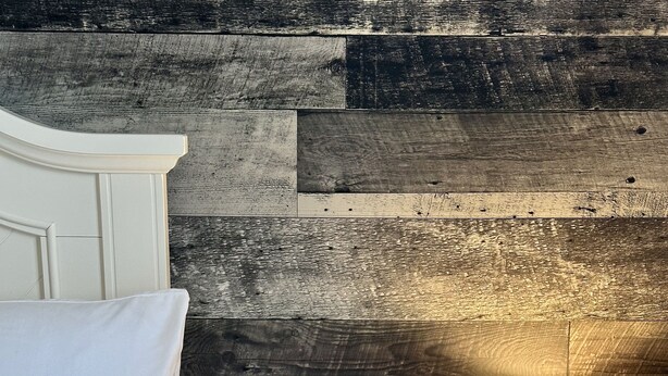 Uma cama bem arrumada com travesseiro e edredom brancos, uma mesa de cabeceira com abajur, caixa de lenços e um pote de petiscos.