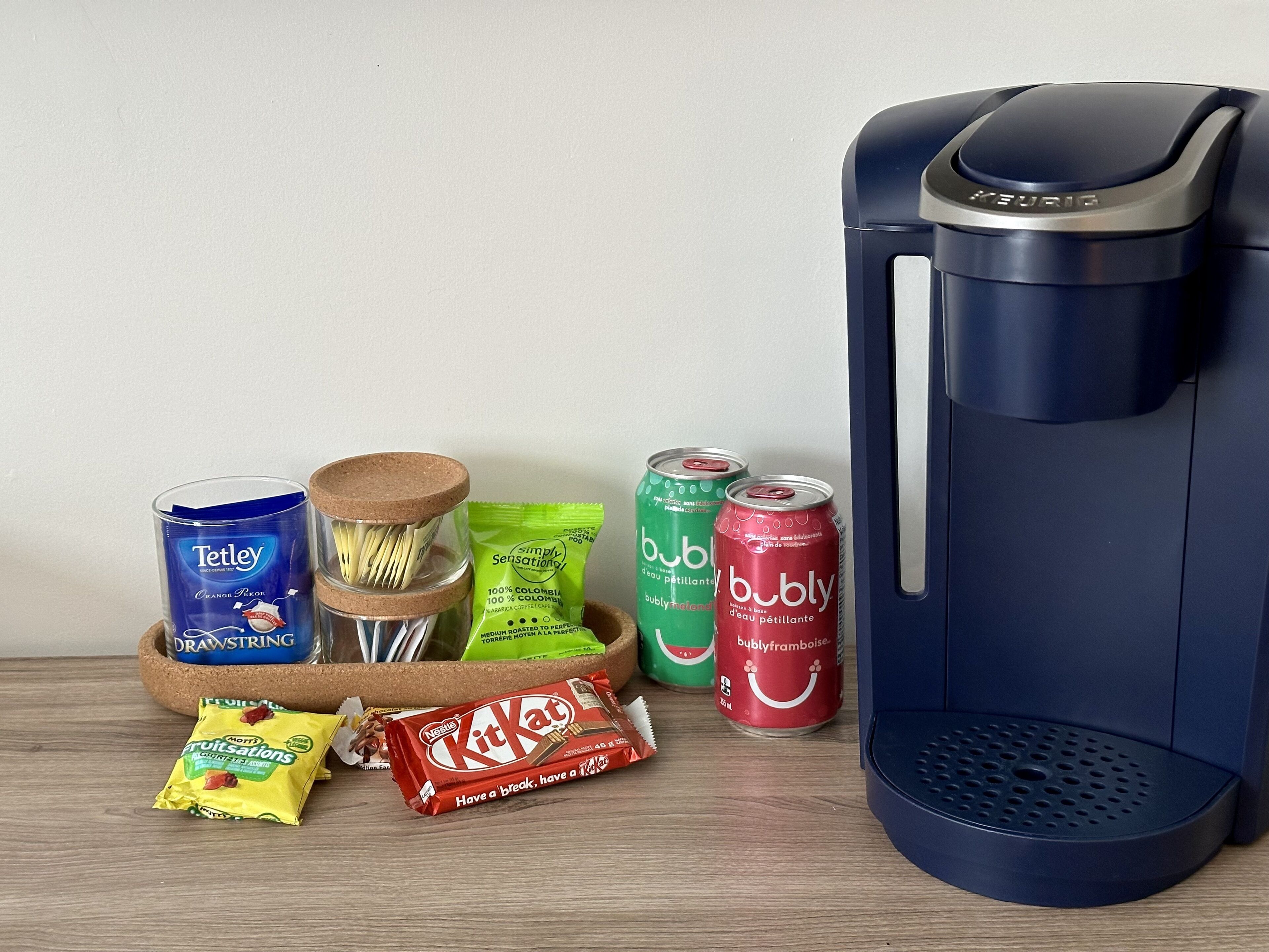 Une machine à café, un verre de thé Tetley, un paquet de barres KitKat et deux canettes de bubly.