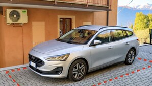 Um SUV prateado estacionado em frente a um prédio com um aparelho de ar condicionado na parede.