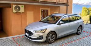 Un vehículo SUV plateado estacionado frente a un edificio con un equipo de aire acondicionado instalado en la pared.