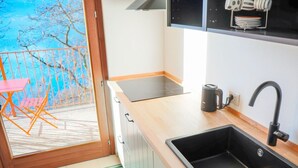Cozinha moderna com pia preta, bancada de madeira e janela com vista para uma varanda com cadeira.