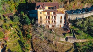 Um edifício com várias andares e varandas, cercado por árvores e um muro de pedra.