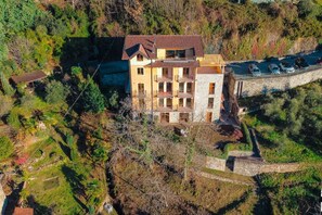 Un edificio de varios pisos con balcones, rodeado de árboles y un muro de piedra.