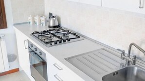 Cuina amb fogó a gas, forn, vàter i armaris blancs.