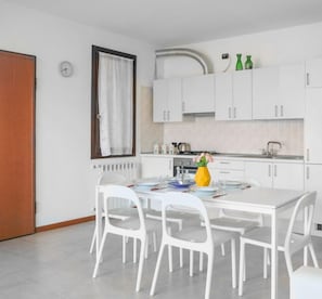 Una cuina moderna amb armaris blancs, taula de menjador amb cadires i finestra amb cortines.