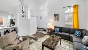 A spacious living room with a grey sofa, a coffee table, and a dining area with a white railing and a kitchen counter. - Frisco Resort Style Home with Spa (Frisco)