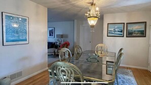 A dining area with a glass table and metal chairs, a chandelier, and framed artwork on the walls.