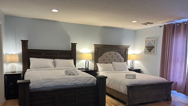 A double room with two beds, wooden headboards, bedside tables with lamps, and a patterned rug.