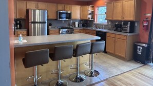 A modern kitchen with wooden cabinets, stainless steel appliances, a central island with bar stools, and a window providing natural light.