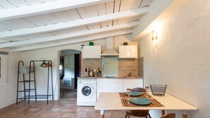 A compact kitchen with a washing machine, a dining table with chairs, and a small seating area.