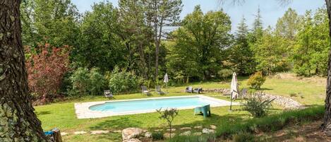 A swimming pool surrounded by a grassy area with trees, a stone wall, and outdoor seating.