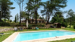 A rectangular swimming pool with a stone border, surrounded by grass and trees.