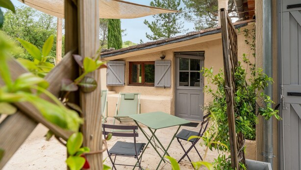 A patio with a table and chairs, a covered area, and a building with a door and windows.