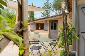 A patio with a table and chairs, a covered area, and a building with a door and windows. - Studio with Pool in the Luberon – Maison Marvic (Apt)
