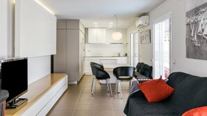 Un saló modern amb un televisor de pantalla plana, un sofà negre amb un coixí vermell, i una zona de menjador amb dues cadires negres.