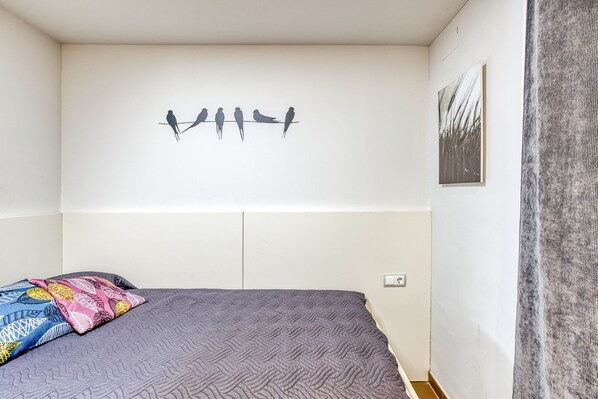 Un dormitorio con cama, un cuadro de aves colgado en la pared, un enchufe y una cortina.