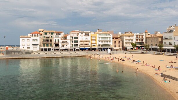 Un poble costaner amb una platja, edificis i un mar tranquil.