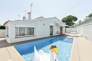 A swimming pool with a swan float, a white building with large windows, and a tiled deck.
