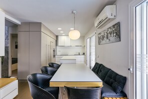 Una cocina moderna con una isla central, iluminación empotrada y una zona de comedor con sillas y un banco.