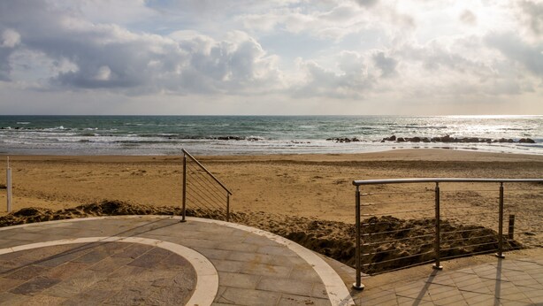 A beach with a curved stone pathway leading to the water, metal railings, and a cloudy sky. - Apartment 'Casa Montecristo' with Air Conditioning, 50 Meters from the Sea (Castiglione della Pescaia)