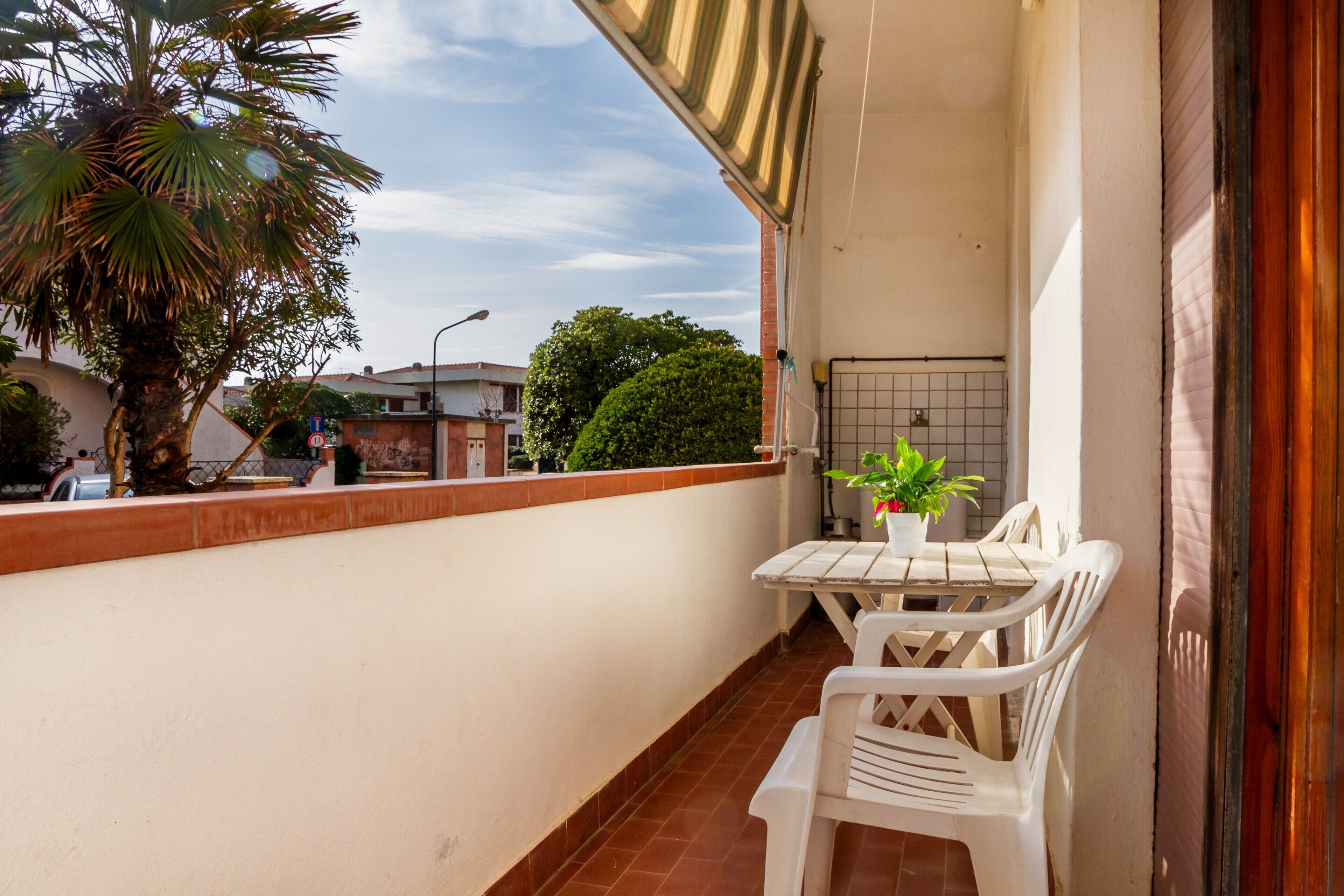 A balcony with a white table and chairs, a potted plant, and a view of the street and buildings.