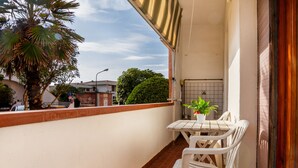 A balcony with a white table and chairs, a potted plant, and a view of the street and buildings. - Apartment 'Casa Montecristo' with Air Conditioning, 50 Meters from the Sea (Castiglione della Pescaia)