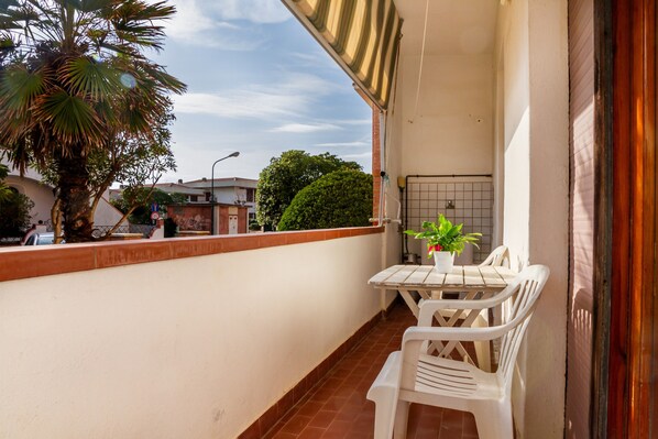 A balcony with a white table and chairs, a potted plant, and a view of the street and buildings.